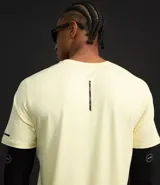 Remera deportiva de hombre con tecnología dry fit, cuello redondo y manga corta. Presenta un diseño liso en color beige con una pequeña etiqueta decorativa en el dobladillo.