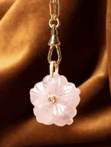 Dije con forma de flor tallado en cuarzo rosa, con una pequeña circonia incrustada en el centro y engarce de metal dorado.