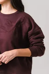 Buzo de cuello redondo en color bordó, con diseño de bordado floral en la parte superior del pecho y mangas largas con puños acanalados.