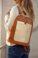 Mochila de cuero color tostado con bolsillo frontal dorado y cierre plateado.