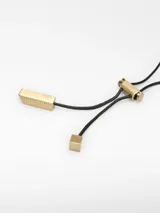 Collar largo con cordón negro regulable y colgante compuesto por dos piezas metálicas irregulares entrelazadas en acabados dorado y plateado.