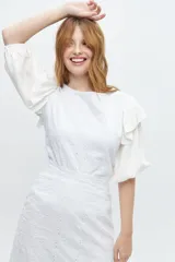 Blusa blanca con mangas abullonadas y volados en las sisas. El cuerpo de la blusa es de tela bordada con pequeños orificios.