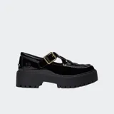 Zapato tipo Mary Jane de charol negro con plataforma gruesa y suela track. Presenta un diseño de tira con hebilla dorada y costuras blancas decorativas en la puntera. Incluye el logo de Timberland grabado en el talón.