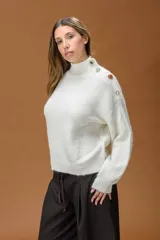 Polera de punto color blanco, de corte relajado y cuello alto. Presenta detalle de botones joya decorativos en uno de los hombros.