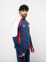 Buzo de entrenamiento Umbro del Club Nacional de Football, con cierre frontal parcial y cuello alto. Presenta un diseño con bloques de color azul, blanco y rojo, con panel frontal acolchado y mangas largas con aberturas para pulgares.