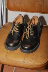 Borcego de cuero en tono marrón oscuro con efecto desgastado, cordones bicolor y suela track dentada de goma negra.