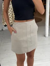 Pollera corta de cuero sintético con diseño de paneles y bolsillos frontales grandes. Presenta un corte recto y tiro medio.