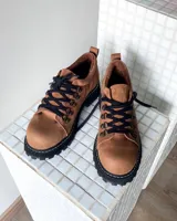 Zapatos tipo borceguíes bajos de cuero vacuno color tostado, con suela track negra de goma y cordones negros con ganchos metálicos.