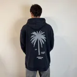 Canguro negro con capucha y cordones ajustables, de corte oversize. Estampado en la espalda con una palmera gris, el logo de la marca y la frase "surf n' destroy praise the sea to it's edge".