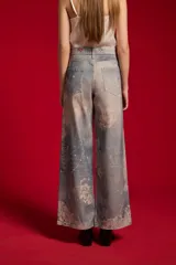 Pantalón jean de tiro medio y corte ancho, con estampado artístico en tonos celestes y blancos.
