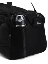 Bolso deportivo Under Armour Undeniable 5.0 Medium, color negro con el logo de la marca en blanco. Cuenta con tecnología UA Storm resistente al agua, compartimento principal con cierre, bolsillo ventilado para ropa sucia o calzado, bolsillos laterales para botellas y correa de hombro ajustable y acolchada.