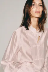 Camisa satinada de manga larga con cuello redondo y cierre frontal con alamares. Cuenta con bolsillos de plastrón en el frente y diseño de corte recto.