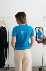 Remera de algodón blanca, con cuello redondo y mangas cortas. Presenta un estampado frontal con la palabra "KAPSUL" en rojo sobre un diseño floral en tono beige.