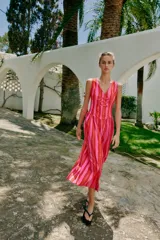 Vestido largo sin mangas con escote en pico y tirantes anchos. Presenta un diseño de rayas verticales en tonos fucsia y rojo, con detalle de falsos botones frontales y cierre de cremallera oculto en la espalda.