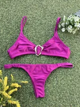 Bikini de tela metalizada color magenta, compuesto por un top con breteles finos y detalle de hebilla metálica en el centro, y una bombacha tipo colaless.