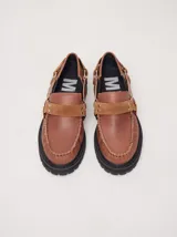 Mocasines Mutma Gales de cuero color tostado, con plataforma gruesa dentada, detalles de tachas metálicas, argollas y tira lateral con hebilla.