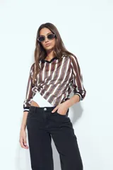 Remera de manga larga con tejido tipo mesh, diseño de rayas verticales en tonos marrones y blancos, cuello polo negro y puños tejidos con detalle de rayas.