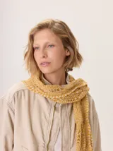 Bufanda tejida de lana, color amarillo mostaza con detalles en blanco, con textura calada y flecos en los extremos.