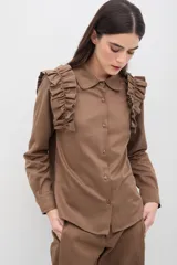 Camisa de manga larga color marrón, con cuello clásico y detalle de volados en los hombros. Presenta cierre frontal con botones al tono.