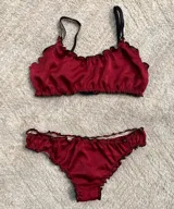 Conjunto de lencería compuesto por un corpiño tipo bralette y una bombacha colaless, confeccionados en satén color crema con terminaciones fruncidas. El corpiño cuenta con breteles regulables y doble capa de tela, mientras que la bombacha presenta un diseño de corte cavado con elásticos suaves.