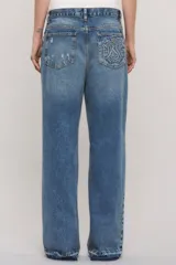 Jeans de denim azul con calce holgado y tiro medio, con diseño de cintura asimétrica cruzada, roturas localizadas y ruedo desflecado con degradé.
