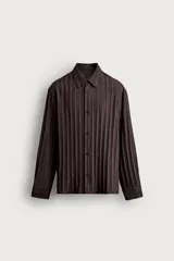 Camisa de manga larga con ajuste relajado, confeccionada en tejido de viscosa con textura de rayas verticales. Presenta cuello camisero, cierre frontal de botones y aberturas en el bajo lateral.