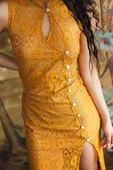 Vestido largo mostaza de encaje, con diseño entallado al cuerpo, cuello alto, abertura frontal en el escote y cierre lateral con botones blancos. Presenta tajo en la pierna.