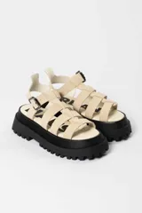 Sandalia tipo gladiadora con plataforma track negra. Presenta un diseño bicolor con tiras delanteras en color amarillo neón y talón con tira ajustable en color beige. Incluye hebilla metálica negra.