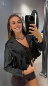 Campera corta de cuero sintético negro con diseño de flecos en el frente y mangas. Presenta cuello solapa y cierre frontal.