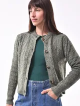 Cárdigan tejido color gris claro con diseño trenzado, cuello redondo y cierre frontal con botones marrones.