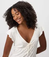 Pijama corto de dos piezas en color blanco con estampado continuo de pequeños corazones rosados. Incluye una blusa con escote en V, mangas cortas con volados, lazo frontal bajo el busto y un short con cintura elastizada y volados en los bajos.