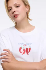 Remera de corte oversized en color blanco, con cuello redondo y mangas cortas. Presenta una estampa central con la frase 'Living a hot life' y un diseño de ajíes rojos.