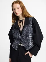 Chaleco con frente cubierto de lentejuelas en tono gris metálico y espalda confeccionada en tela viscosa lisa color negro. Posee escote en V y un diseño liviano pensado para ocasiones de fiesta o para elevar un look casual.