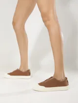 Sneaker slip-on Schutz color camel, confeccionada en lona con bordes deshilachados y suela de goma blanca con textura estriada en la puntera.