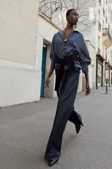 Camisa de rayas verticales azules y blancas, de cuello solapa con escote en V y cierre frontal con botones. Presenta mangas abullonadas por debajo del codo.