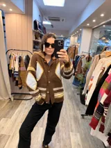 Campera tejida de punto en color marrón con diseño de rombos en tonos celestes y amarillos. Presenta cuello con detalle de corderito, cierre frontal con botones y puños acanalados.