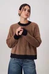 Sweater de tejido suave con textura peluda, de corte holgado y manga larga. Presenta un diseño bicolor con cuerpo en tono beige melange y terminaciones en cuello, puños y ruedo en color negro.