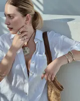 Collar artesanal con dije central de metal con textura orgánica irregular que evoca una ostra. El dije está montado sobre un cordón de algodón natural, permitiendo un uso versátil y regulable.