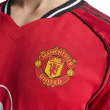 Camiseta de fútbol Adidas del Manchester United, modelo Local 25/26. Diseño rojo con detalles negros y blancos en cuello y mangas. Incluye logo de Adidas, escudo del club y sponsor Snapdragon en el frente.