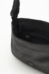 Cartera de mano tipo baguette confeccionada en cuero vacuno negro, con solapa decorada mediante diseño calado y tachas metálicas. Presenta una correa trenzada y un pañuelo estampado anudado en uno de sus laterales.