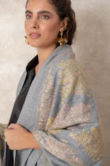 Pashmina de tela densa y suave, con caída pesada y diseño bordado con motivos florales en tonos dorados y beige. Presenta terminaciones con flecos en los extremos.