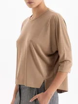 Remera de silueta relajada confeccionada en tela de punto suave. Presenta escote redondo, mangas 3/4, recorte estratégico en la espalda y tajos laterales que aportan movimiento y una caída fluida.