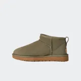 Botas de caña baja UGG modelo Classic Ultra Mini, color negro. Confeccionadas en piel de oveja con forro interior de lana, cuentan con una línea superior asimétrica, costuras decorativas y suela flexible y liviana.