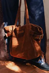 Bolso tipo shopper confeccionado en cuero descarne color marrón, con diseño de flecos en los laterales y correas ajustables con hebillas metálicas. Incluye doble bolsillo interno y tira porta llaves.