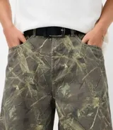 Bermuda de corte baggy confeccionada en sarga de algodón con estampado camuflado. Presenta cintura con trabillas, cierre frontal tradicional y bolsillos funcionales en la parte delantera y trasera.