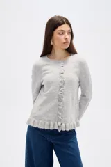 Saco de punto color gris, con cuello redondo, cierre frontal con botones y detalle de volados en la tapeta y el ruedo. Presenta mangas largas con puños acampanados.