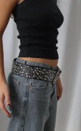 Cinto negro de cuero sintético con diseño de múltiples tachas metálicas circulares y hebilla plateada.