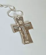 Collar con dije de cruz de diseño artesanal con acabado irregular y calado central, suspendido de una cadena tipo serpiente. El dije presenta tres pequeñas incrustaciones de piedras oscuras en la parte superior.