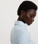 Blusa tipo polo de manga larga, confeccionada en tejido interlock de algodón y poliéster. Presenta cuello clásico con cierre frontal de botones y diseño básico liso.