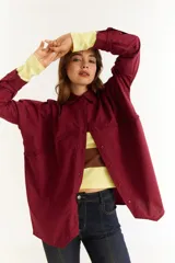 Camisa de corte oversize color bordó, con cuello clásico, cierre frontal de botones y detalle de trenzado horizontal en la parte superior delantera. Posee mangas largas con puños abotonados.